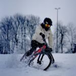 man in white jacket riding on black bmx bike on snow covered ground during daytime